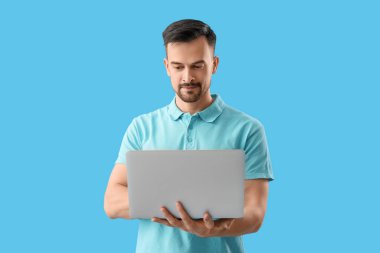 Mavi arka planda dizüstü bilgisayar kullanan yakışıklı adam.