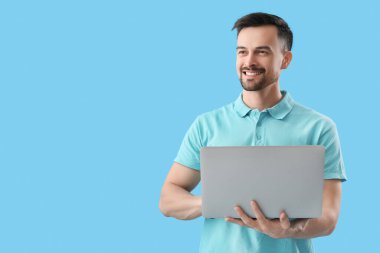 Mavi arka planda dizüstü bilgisayar kullanan yakışıklı adam.