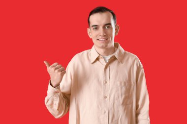 Genç adam kırmızı arka plandaki bir şeyi işaret ediyor.