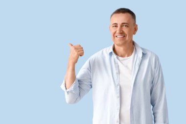 Olgun adam mavi arka plandaki bir şeyi işaret ediyor.