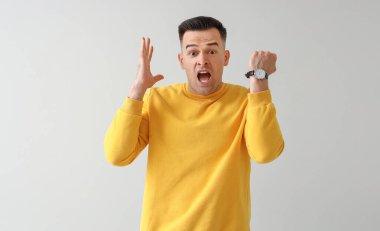 Hafif arka planda kol saati olan stresli genç bir adam. Son teslim tarihi kavramı