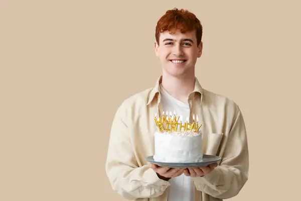 Young man with birthday cake on beige background