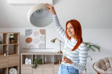 Güzel genç bir kadın evinde ampulü değiştiriyor.