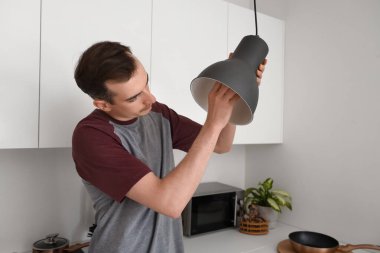 Genç adam mutfakta ampul değiştiriyor.