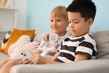 Evdeki kanepede cep telefonuyla oynayan şirin çocuklar.