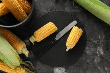 Siyah masada taze mısır koçanı ve yemek var.