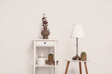 Tuvalet masasında okaliptüs dalları ve beyaz duvarın yanında lamba olan vazo.