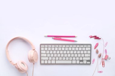 Beyaz arkaplanda modern bilgisayar klavyesi, kulaklık ve kırtasiye malzemesi kompozisyonu