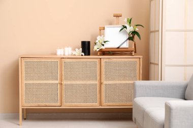 İçinde zambak çiçekleri olan boş bir cenaze çerçevesi, morg vazosu ve renkli duvarlara karşı ahşap dolapta yanan mumlar.