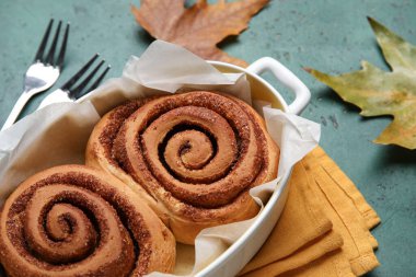 Lezzetli tarçınlı çörekler ve yeşil arka planda sonbahar yaprakları.