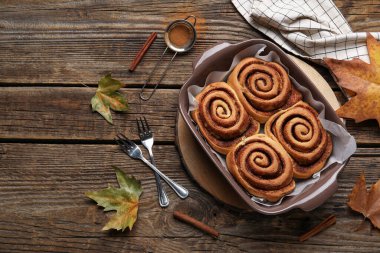 Ahşap zemin üzerinde lezzetli tarçın ruloları ve sonbahar yaprakları pişirme yemeği