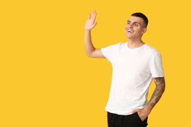 Sarı arka planda el sallayan yakışıklı genç adam.
