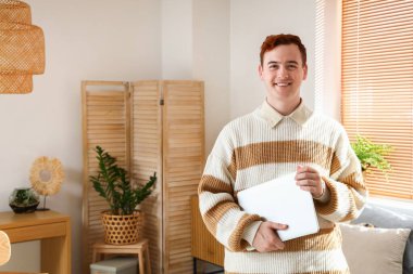 Evde dizüstü bilgisayarı olan mutlu, kızıl saçlı genç bir adam.