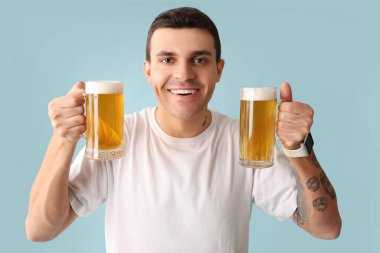 Mavi arka planda bir kupa birası olan yakışıklı genç adam.