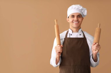 Kahverengi arka planda merdaneleri olan yakışıklı, mutlu bir aşçı.