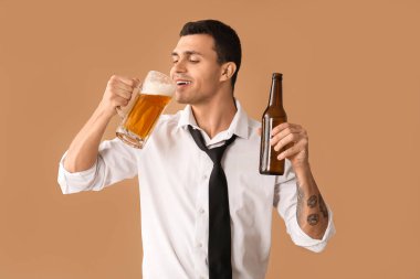 Kahverengi arka planda bir kupa birası ve şişesi olan yakışıklı bir genç.