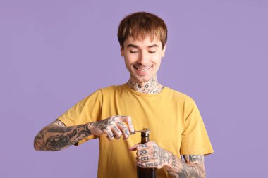 Dövmeli genç mutlu adam mor arka planda bira şişesi açıyor.