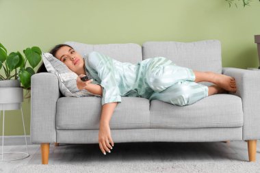 Güzel, genç, sıkılmış bir kadın kanepede uzanıyor ve yeşil duvarın yanında televizyon izliyor.