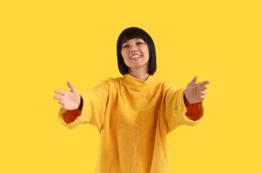 Sarı arka planda sarılmak için kollarını açan genç kadın.