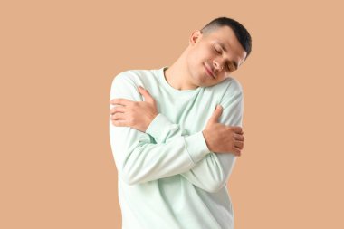 Bej arka planda kendine sarılan genç adam.