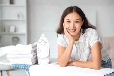 Genç Asyalı kadın ütü masasına yaslanıyor.