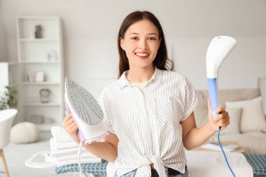 Evde demir ve giysi buharlı genç bir Asyalı kadın var.