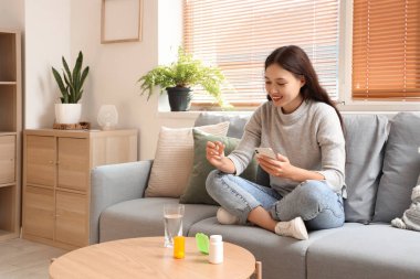 Genç Asyalı kadın evde internetten hap tarifine bakıyor.