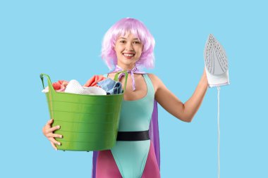 Mavi arka planda demir ve sepet dolu süper kahraman gibi giyinmiş genç bir kadın.