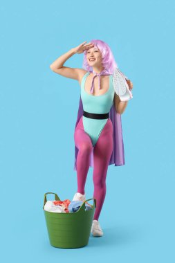 Mavi arka planda demir ve sepet dolu süper kahraman gibi giyinmiş genç bir kadın.