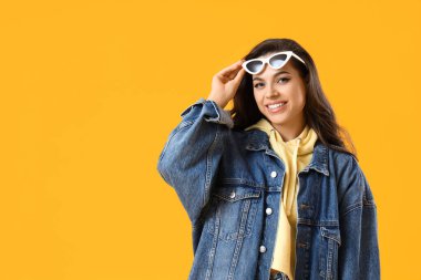 Sarı arka planda şık güneş gözlüklü güzel bir genç bayan.