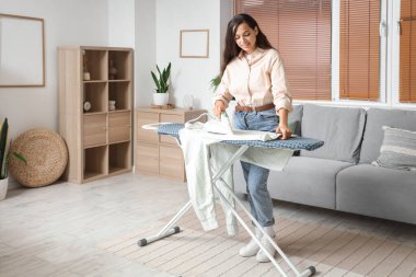 Güzel genç bayan evde giysileri ütülüyor.