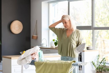 Ütülü, yorgun ve olgun bir kadın evdeki giysilere bakıyor.