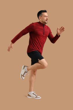 Spor giyim sektöründe kahverengi arka planda koşan yakışıklı bir genç.