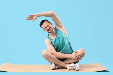 Mavi arka planda yoga minderiyle spor giyim sektöründe yakışıklı genç bir adam.
