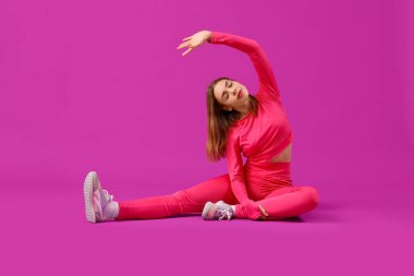 Spor giyimli güzel bir kadın mor arka planda geriniyor.