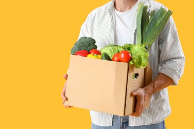 Sarı arka planda bir kutu taze sebzeli olgun adam, yakın plan.