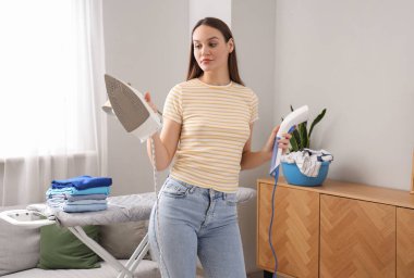 Güzel bir genç kadın evde demir ve giysi buharı arasında seçim yapıyor.