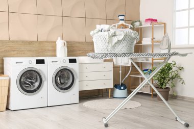 Çağdaş demir ve sepet dolu ütü tahtası çamaşır odasında.