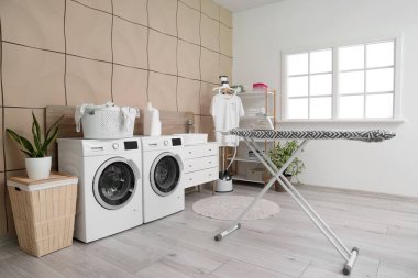 Çamaşır odasında modern demirle ütü tahtası.