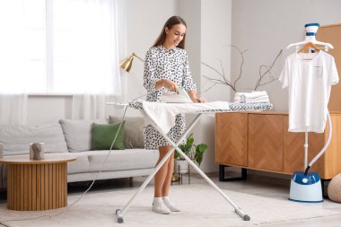 Güzel genç bayan evde giysileri ütülüyor.