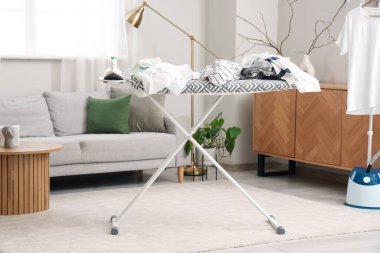 Modern demirle ütü masası ve elbise yığını oturma odasında.