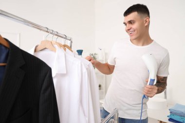 Buharlı tenceresi ve elbise askısı olan mutlu genç bir adam.