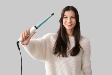 Gri arka planda saç maşası olan güzel, mutlu bir kadın.