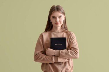 İncil 'i olan genç bir kadın yeşil arka planda dua ediyor.