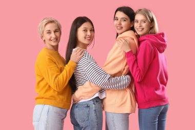 Farklı yaşlarda güzel kadınlar pembe arka planda sarılıyorlar.