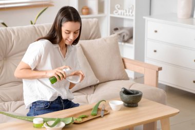 Güzel, genç, mutlu bir kadın oturma odasında aloe vera jeli yapıyor.