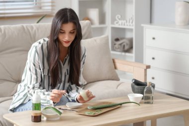 Güzel genç bir kadın oturma odasında aloe vera 'dan gerekli yağı yapıyor.