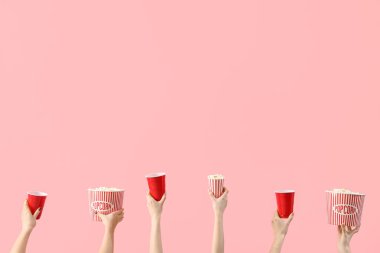 Patlamış mısırlı kovaları tutan eller ve pembe arka planda içkiler