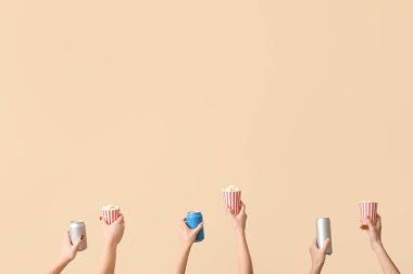 Kovaları patlamış mısırla tutan eller ve bej arka planda içkiler