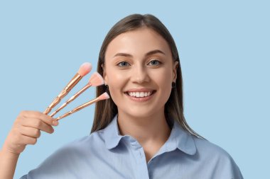 Mavi arka planda makyaj fırçası olan güzel bir kadın, yakın plan.